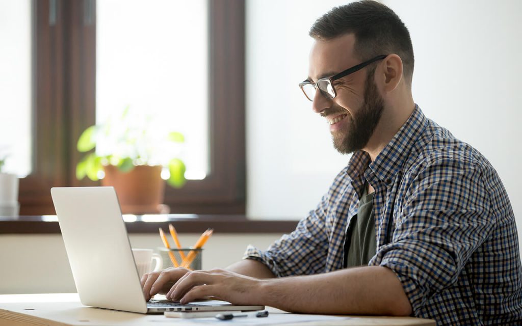 Jovem alegre a frente de seu notebook trabalhando em estratégias de vendas por e-mail